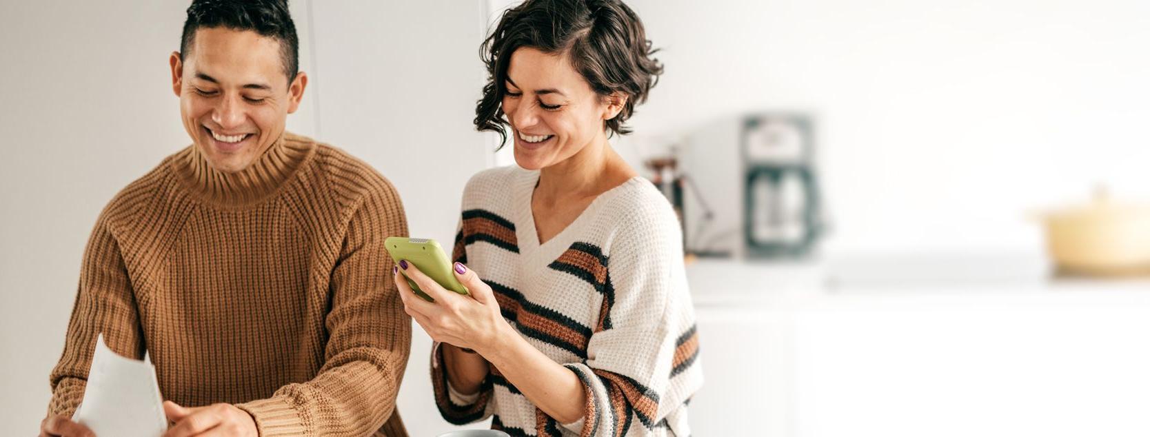 A smiling woman checks her IRA account from Patelco's mobile app as a man sorts papers.