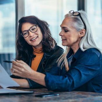 Two smiling women review financial paperwork.