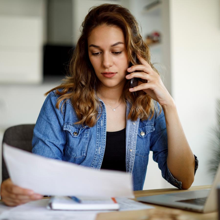 Patelco member at the kitchen table holding up a mobile device and looking at a bill.